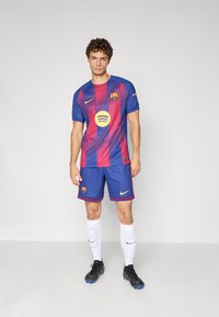 Echipamentul de fotbal al FC Barcelona, în culori albastre și roșii cu dungi verticale, având un logo proeminent Spotify, marcă Nike și șorturi asortate.