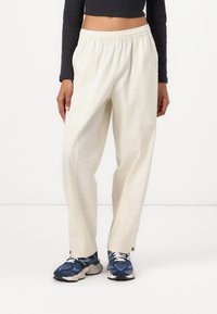 Lysebeige, løstsittende bukser med elastisk midjebånd, med sidelommer og subtil tekstur. Brukt med blå og hvite sneakers.