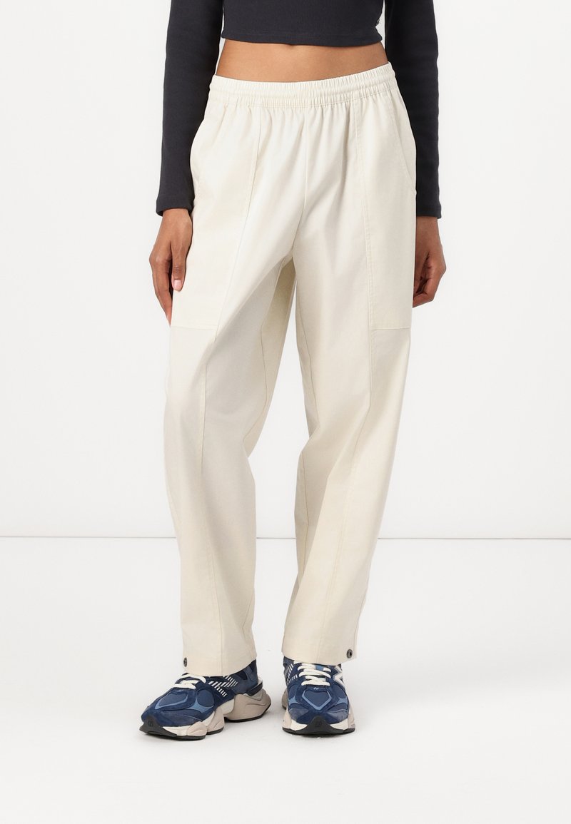 Lysebeige, løstsittende bukser med elastisk midjebånd, med sidelommer og subtil tekstur. Brukt med blå og hvite sneakers.