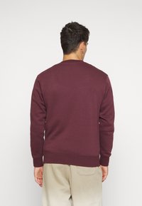 Burgundy sweatshirt with long sleeves and ribbed cuffs. Features a classic crew neckline and soft texture. Visible hemline at the waist.