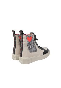 Sneakers alte in suede beige con punta in pelle nera. Presentano una stampa leopardata e accenti a forma di cuore rossi sui lati, con suola in gomma nera texture.