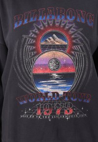Felpa nera con grafica multicolore che presenta montagne, una galassia e acqua. Il testo recita "BILLABONG WORLD TOUR 1973."