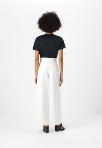 Camiseta negra de manga corta combinada con pantalones de pierna ancha blancos de cintura alta. Los pantalones cuentan con dos bolsillos traseros y una cinturilla texturizada.