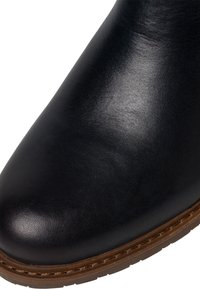 Stivale alla caviglia in pelle nera con texture liscia, punta rotonda e suola marrone chiaro in contrasto con dettagli di cucitura.