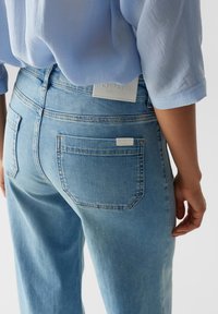 Light blue denim jeans with a relaxed fit, featuring two back pockets and a subtle brand tag at the waistband. Smooth texture.