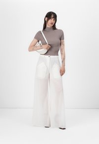 Brun ribbad kortärmad topp i kombination med vita vida byxor med stora framfickor. Modellen håller en liten vit väska.