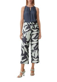 Mouwloos donkerblauw top met een sleutelgatontwerp; brede broek met een groen botanisch patroon op een donkere achtergrond; lichtgroene hakken.