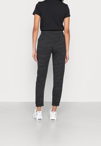 Svarta, åtsittande sweatpants med en strukturerad väv. Manschetter och elastisk midja. Kombinerat med vita sportskor.