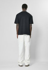 Juoda per didelė t-shirt su trumpomis rankovėmis, pagaminta iš medvilnės, derinama su baltais plačiais kelnėmis, paprasto dizaino, be matomų logotipų ar raštų.