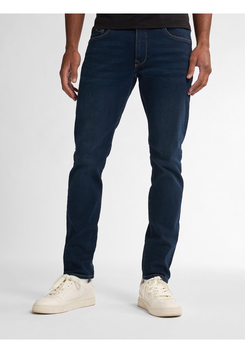 Tmavě modré džíny slim fit s předními kapsami, jemnými detaily whiskering a kombinované s krémovými teniskami.