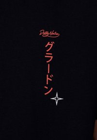 Schwarzes Baumwoll-T-Shirt mit rotem und weißem Drucktext "Dolly Noire" und japanischen Zeichen, darunter mit einem Sternakzent.