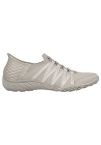 Baskets de sport gris clair avec un talon texturé, des sangles élastiques, un tissu lisse et une semelle flexible dotée de motifs de grip.