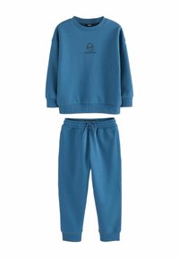 Blå sweatshirt og matchende joggingbukser lavet af blødt materiale. Sweatshirten har en rund hals og et logo-design; joggingbukserne har en elastisk talje.
