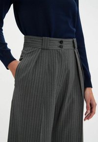 Pantalons à rayures grises avec une coupe ajustée, dotés d'une taille haute, de deux boutons et d'un design à l'avant plat. Tissu texturé avec des plis.