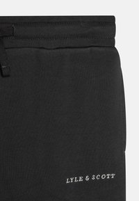 Fekete pamut joggerek textúrált felülettel, elasztikus derékkal és megkötő zsinórral. A "LYLE & SCOTT" logó fehér színben a szegély alján található.
