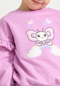 Felpa rosa con una grafica di farfalla, arcobaleno e nuvole. Maniche arricciate, texture morbida e dettagli di cuori giocosi in colori tenui.