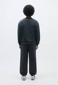 Sudadera gris oscuro con puños y dobladillo acanalados, combinada con pantalones holgados a juego, que cuentan con un bolsillo trasero y una cinturilla elástica.