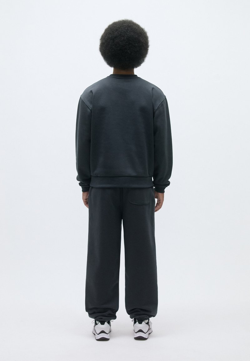 Sweatshirt gris foncé avec des poignets et un ourlet côtelés, associé à un pantalon ample assorti, doté d'une poche arrière et d'une taille élastique.