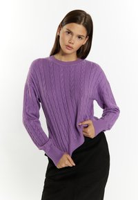 Maglione a maglia a trecce viola con scollo rotondo, vestibilità ampia, polsini a coste e un motivo testurizzato, abbinato a una gonna nera.