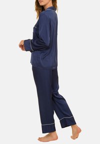 Ensemble de pyjama en satin bleu marine avec des manches longues et un pantalon, doté de bordures blanches le long du col et des poignets. Texture douce, coupe décontractée.
