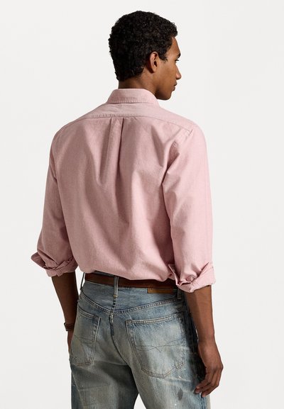 Ljusrosa långärmad skjorta med uppvikta ärmslut, ryggsöm och subtil textur, kombinerad med urtvättade blå jeans med slitna detaljer.