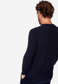 Maglione lavorato a maglia blu navy con maniche lunghe e scollatura a girocollo. Texture liscia con un motivo uniforme, design aderente e polsini e orlo a coste.