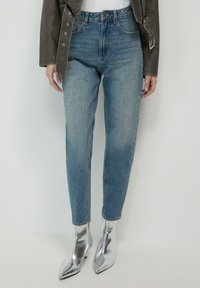 Jean en denim bleu taille haute avec un léger délavage, coupe droite, associés à des bottines argentées à talons aigus.