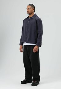 Marineblauw casual jasje met een kraag, knopen aan de voorkant en twee zijzakken, gecombineerd met losse zwarte jeans en chunky schoenen.