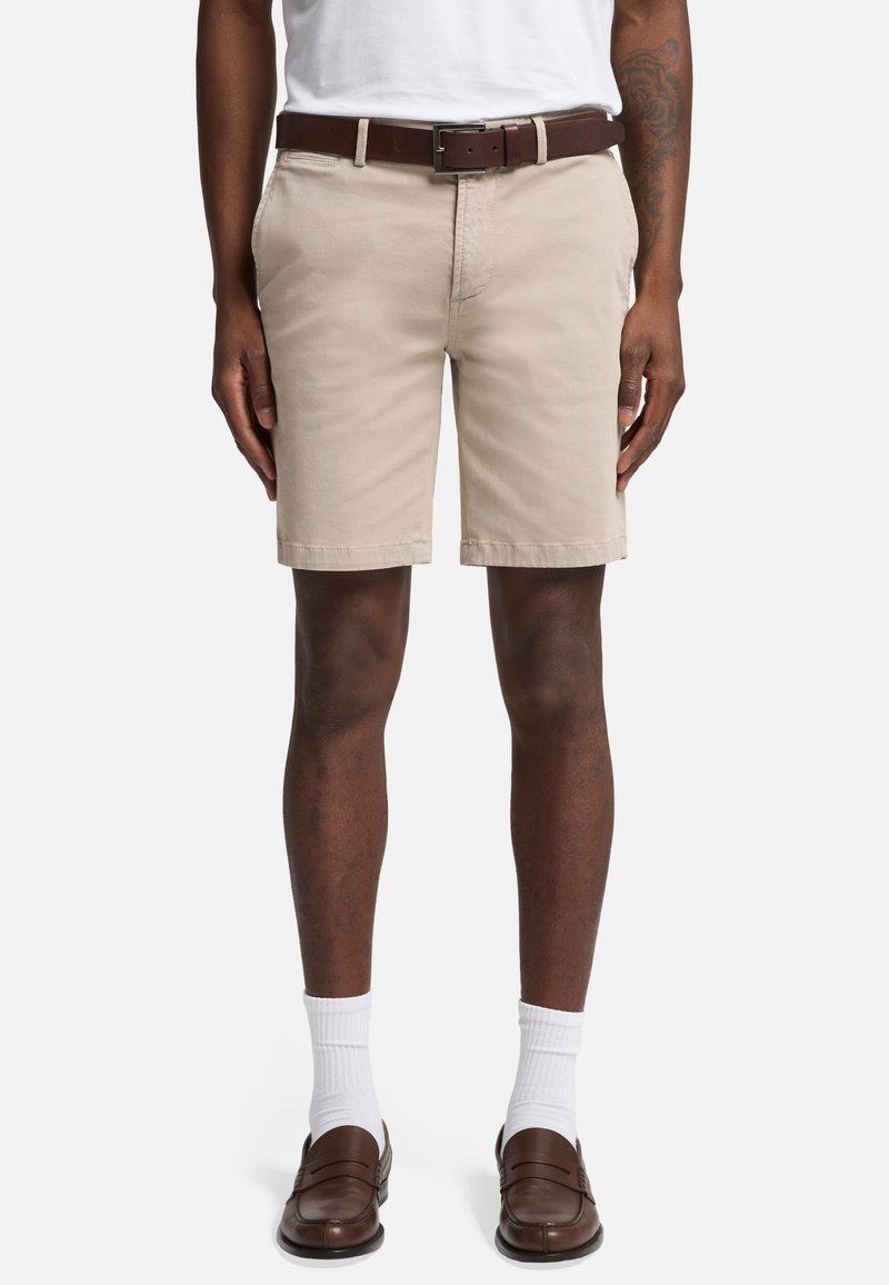 Khaki shorts lavet af bomuld med flad frontdesign, der har sidelommer, et brunt læderbælte, og som er parret med brune slip-on sko og hvide sokker.