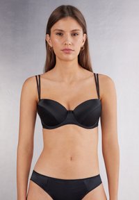 Zwarte beha met beugel en dunne bandjes, met een gladde satijnen afwerking en gevormde cups. Gecombineerd met bijpassende bikinislips.