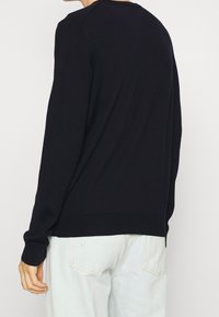 Granatowy sweter dzianinowy z okrągłym dekoltem, prążkowanymi mankietami i dolnym obszyciem, o gładkiej fakturze i luźnym kroju.