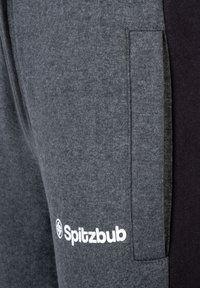 Graue Jogginghose aus weichem Stoff mit Seitentasche und dunkelgrauen Akzenten. Mit weißem "Spitzbub"-Logo auf der unteren linken Seite.