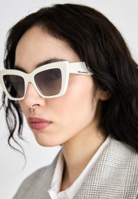Bijele, prevelike mačje sunčane naočale s tamnim gradijentnim staklima i mat finišem. Na krakovima se nalazi logo "Karl Lagerfeld".