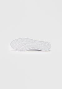 Sola de sapato Puma branca com padrão de aderência circular e design de sulco curvado sobre um fundo branco liso.