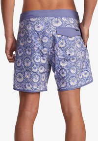 Bañador morado con un patrón floral, bolsillo trasero y cinturilla elástica. Presenta una tela texturizada y costuras en contraste.