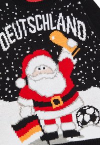 Knittröja med jultomten i röd och vit färg som håller en trofé, med snöflingor på svart bakgrund. Texten "DEUTSCHLAND" ovanför.