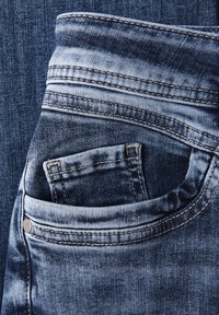 Jeans in denim blu scuro con tasca frontale, caratterizzati da sbiaditure chiare in alcune aree, cuciture a contrasto e un dettaglio con bottone in metallo.
