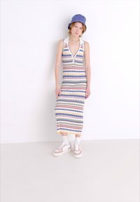 Vestido de punto con rayas verticales en azul, rojo, amarillo y gris, con un escote pronunciado y cierre frontal; combinado con zapatillas blancas.