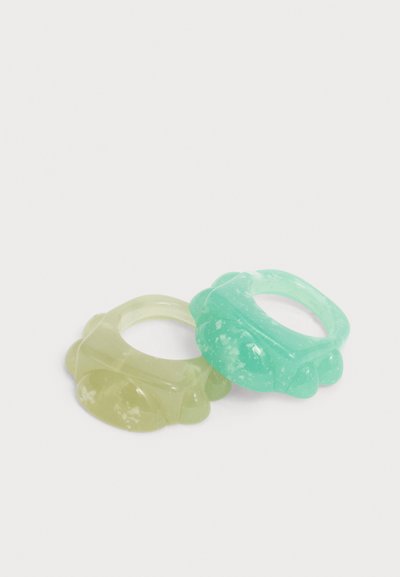 Δύο ημιδιαφανείς δαχτυλίδια από ρητίνη με υφή και ακανόνιστο σχήμα, το ένα ανοιχτό κίτρινο και το άλλο ανοιχτή τιρκουάζ, πάνω σε απλό λευκό φόντο.