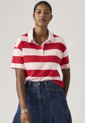 Woman wearing a red and pink wide-striped polo shirt tucked into a high-waisted dark blue denim skirt, accessorized with silver jewelry.