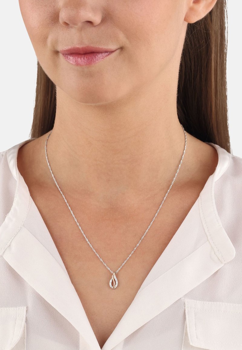 Collana d'argento con pendente a goccia caratterizzato da piccole pietre chiare incastonate, appesa a una catena attorcigliata sopra una blusa bianca.
