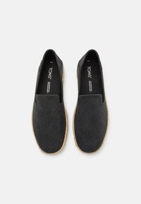 Scarpe slip-on nere in tela con tomaia testurizzata e suola in juta stile espadrille. Presentano un profilo basso e nessun lacci o accessori visibili.