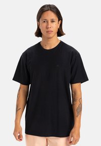 T-shirt in cotone nero con maniche corte, collo rotondo e un piccolo logo sul petto. Tessuto liscio con una vestibilità rilassata.