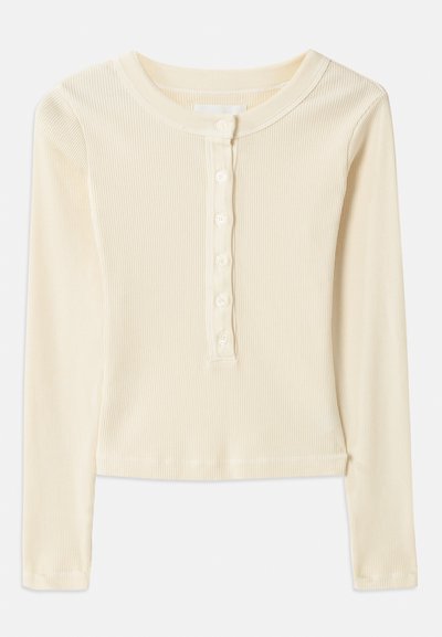 Camisola de manga longa amarelo-claro, com nervuras, e decote redondo, com fecho de seis botões na parte frontal. Possui uma bainha cropped e uma textura suave.