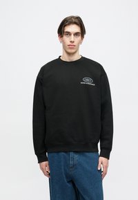 Črna dukserica s okroglo izrezom in rebrastimi manšetami. Na prsih je bel logo in napis "OBEY". Nosi se z modrimi jeans hlačami.