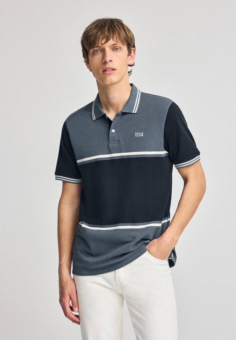 Grå och marinrandig pikétröja med vita accenter, med en treknappslåsning och logotyp på bröstet. Tillverkad av bomullsblandning.