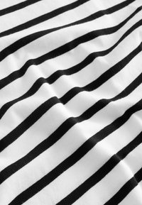 Svartvit randigt tyg med mjuk textur, med växelvis breda och smala ränder, som hänger naturligt med lätt skrynklig yta.