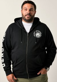 Sort zip-up hoodie lavet af blødt stof, med en frontlomme, snor i hætten samt hvidt logo på brystet og brandet tekst på ærmet.