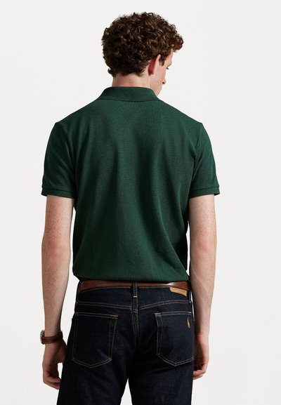 Donkergroene polo met korte mouwen en een klassieke kraag, gecombineerd met donkerdenimjeans. De stof lijkt gestructureerd en heeft een slim fit ontwerp.