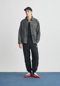 Črno vzorčasto jakno z ovratnikom, združeno s črno srajco, črnimi hlačami in rdečimi supergami z belimi poudarki. Črno kapa dopolnjuje videz.